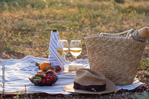 Two glasses of white cheese wine and straw bag bottles, strawberries, straw hat. Summer picnic in nature at sunset. Concept: alcohol and drinks, romantic date. no people, white wine