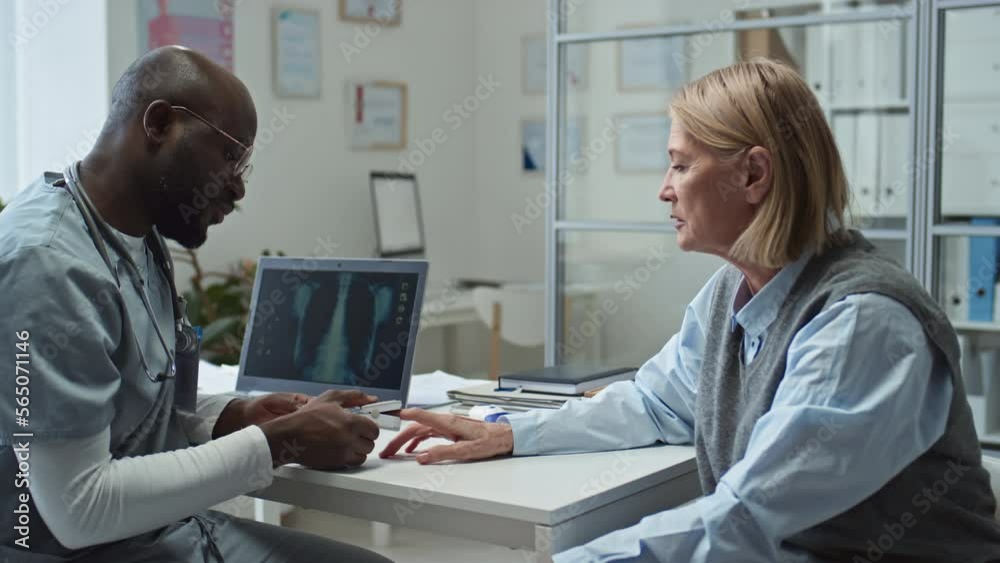 Mature female patient sitting in front of African American general practitioner putting pulse oximeter on her fingertip during check-up of oxygen level in her blood Mature female patient sitting in front of African American general practitioner putting pulse oximeter on her fingertip during check-up of oxygen level in her blood