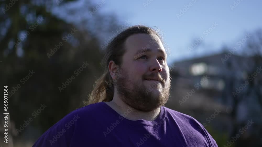 One pensive happy young man walking forward outside smiling. A joyful overweight guy walks outdoors feeling positive. Tracking shot One pensive happy young man walking forward outside smiling. A joyful overweight guy walks outdoors feeling positive. Tracking shot