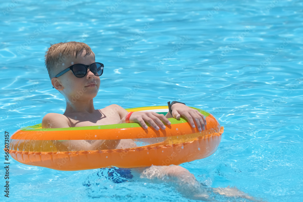 Happy child boy swimming on inflatable circle in swimming pool on sunny summer day during tropical vacations