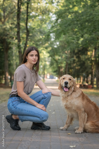Portrait of a young beautiful dark-haired girl with a purebred golden retriever in a summer park.