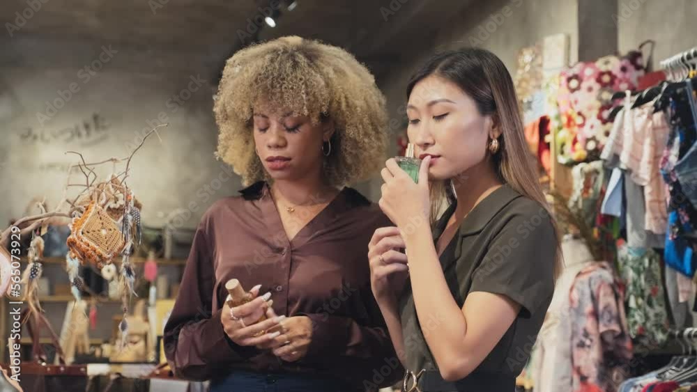 Medium shot of two young women smelling and discussing perfumes while going shopping together in boutique store