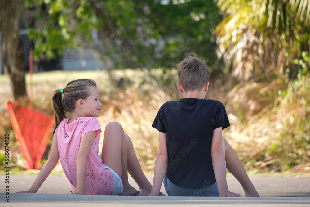 Two happy smiling teenage children, boy and girl sitting outdoors resting, having fun on summer sunny day