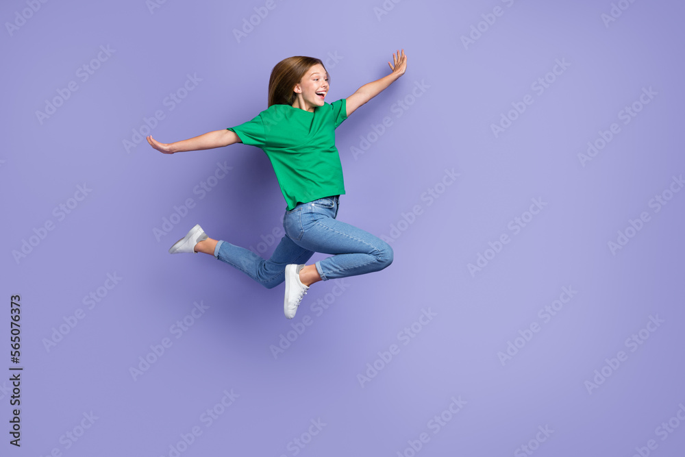 Full length photo of impressed sweet small lady wear green t-shirt jumping high arms sides empty space isolated violet color background