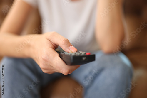 Woman holds remote control in her hand while sitting on sofa.