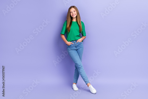 Full length photo of cute cheerful small lady wear green t-shirt smiling walking hand arms pockets isolated violet color background