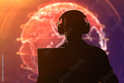 Silhouette of a military man in headphones at a laptop against the background of a glowing globe, contour lighting. Concept: collection of confidential information, surveillance and control of people. photo