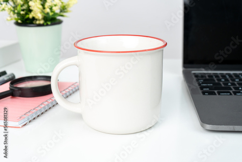 A white blank enamel mug on the top of a white table decorated with tech style