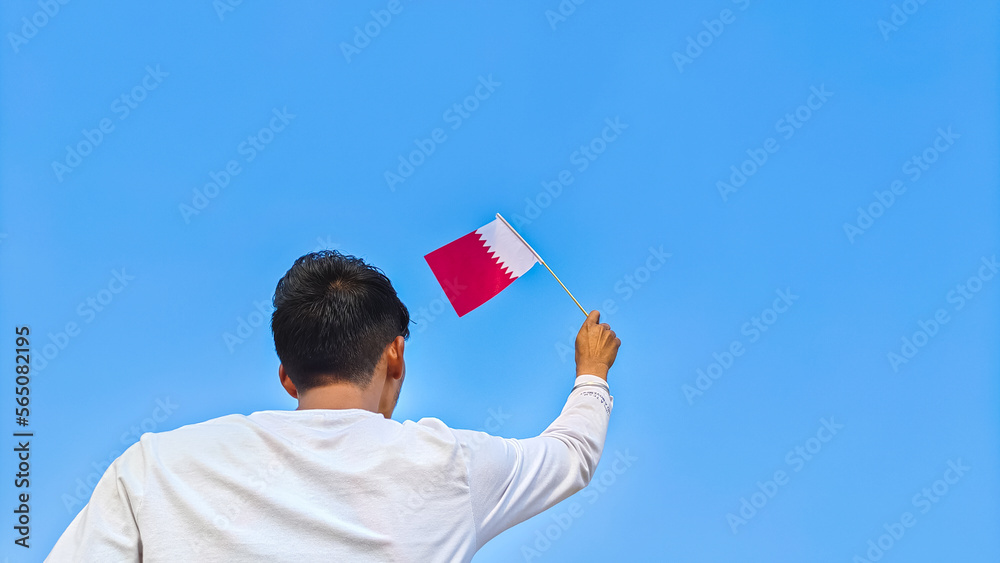 Boy holding Qatar flag against clear blue sky. Man hand waving flag of Qatar view from back, copy space Boy holding Qatar flag against clear blue sky. Man hand waving flag of Qatar view from back, copy space