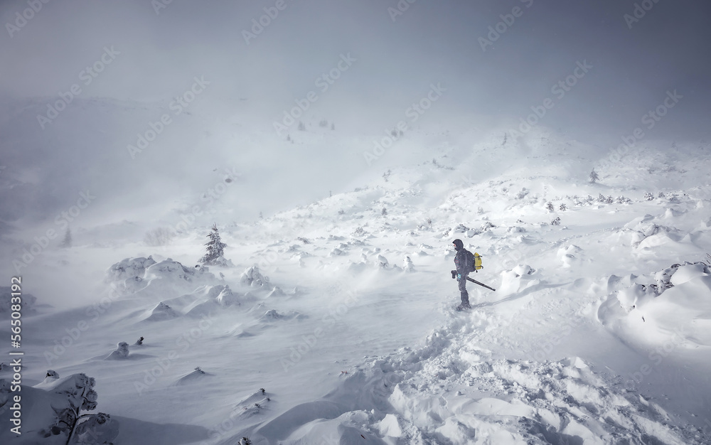 Stunning winter nature landscape. Alone man in snow covered mountain. Hiker, photographer on the snowcapped highland. Outdoors active lifestyle concept. Snowy mountain scenery with cloudy day