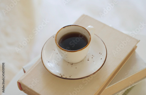 A mug of black coffee stands on a stack of books on the table