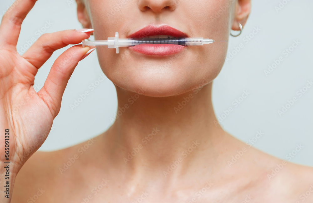 Closeup face young woman holds syringe with hyaluronic in mouth Closeup face young woman holds syringe with hyaluronic in mouth