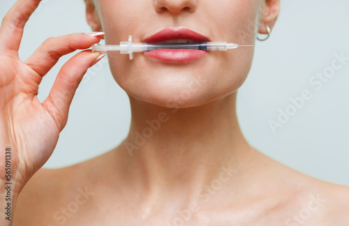 Closeup face young woman holds syringe with hyaluronic  in mouth