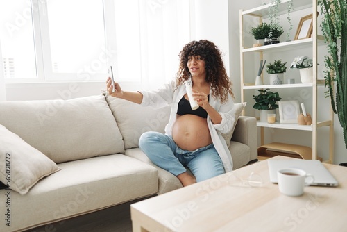A pregnant woman blogger advertises a cream for pregnant women from stretch marks on the body during pregnancy filming herself on the phone while sitting on the couch at home freelancer