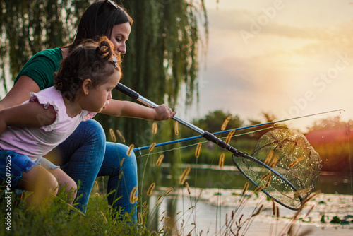 Catching the fish. Mom and daughter trying to catch the fish from the river. Selective focus. Side view.