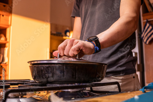 A boy covering a pan with a lid.