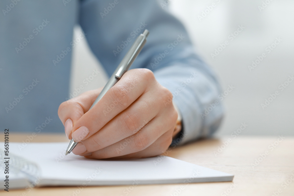 Woman writing in notebook at wooden table, closeup