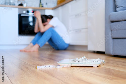 A woman in blue jeans sits on the floor and gets upset about her weight and body. photo