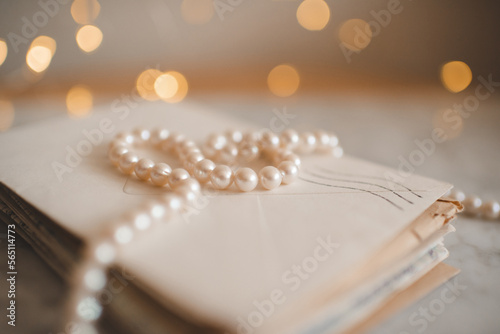 Stack of old paper letters with elegant pearl necklace over glow lights closeup. Selective focus.