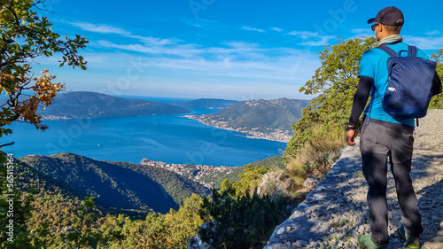 Man with scenic view from mountain summit of Vrmac Sveti Ilija on Kotor bay in summer, Adriatic Mediterranean Sea, Montenegro, Balkans, Europe. Fjord winding along coastal towns. Hiking Dinaric Alps