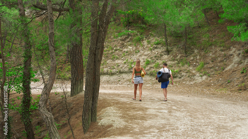 Young people  a man and a woman  walk along a picturesque forest mountain path to the  Blue Abyss  beach. They are holding beach mats in their hands.