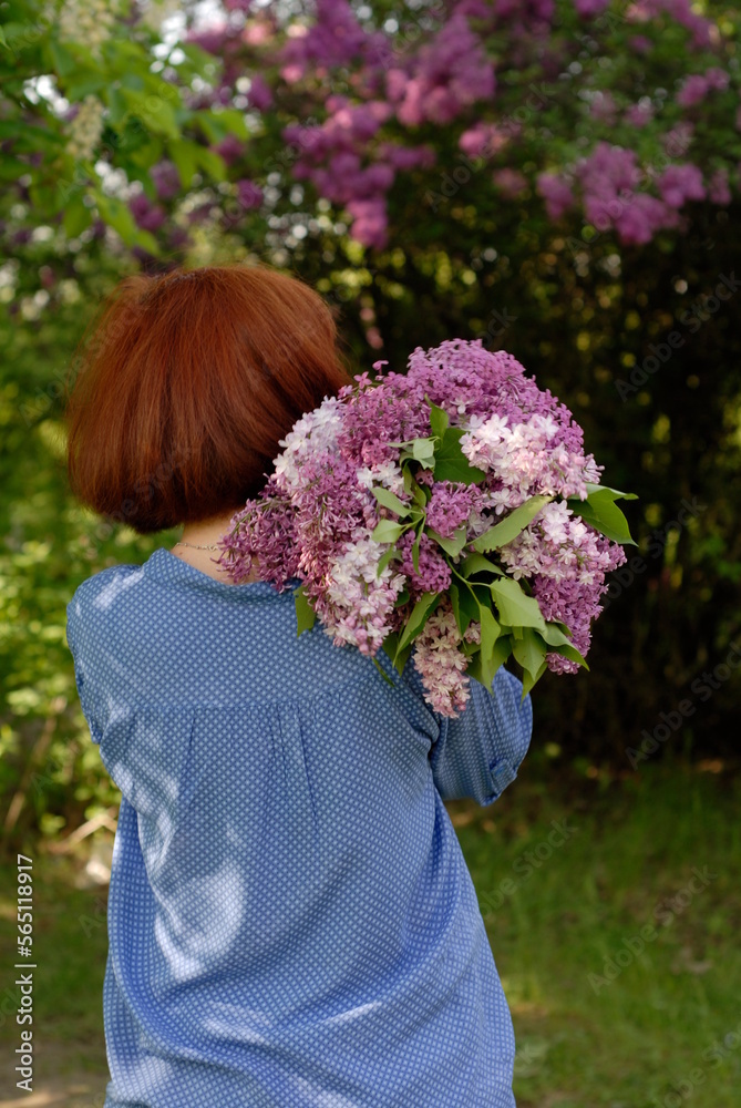 A red-haired girl in a spring park holds a bouquet of lilacs behind her back A red-haired girl in a spring park holds a bouquet of lilacs behind her back