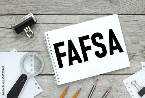 Free Application for Federal Student Aid (FAFSA) concept. wooden background. text on white paper. magnifier and pencils near the notepad. photo