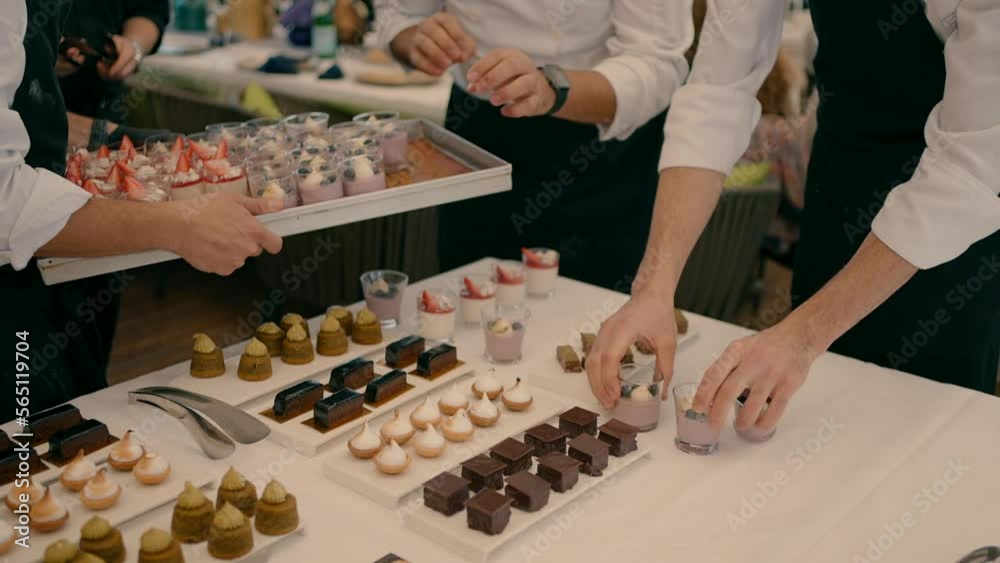Three waiters arrange a variety of desserts on the white table in the buffet.