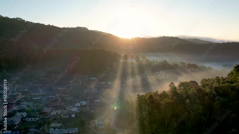 Drone view with fly back over lake at Baan Rak Thai village in Mae Hong Son, Thailand and far from sunrise beam over mountain or hill with fog or mist covering village. Drone view with fly back over lake at Baan Rak Thai village in Mae Hong Son, Thailand and far from sunrise beam over mountain or hill with fog or mist covering village.