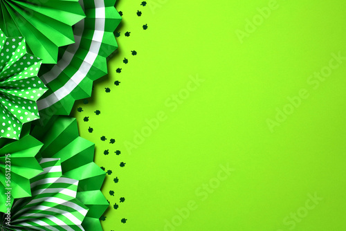 St. Patricks Day background with green folding paper fans and shamrock confetti. Flat lay, top view, copy space.