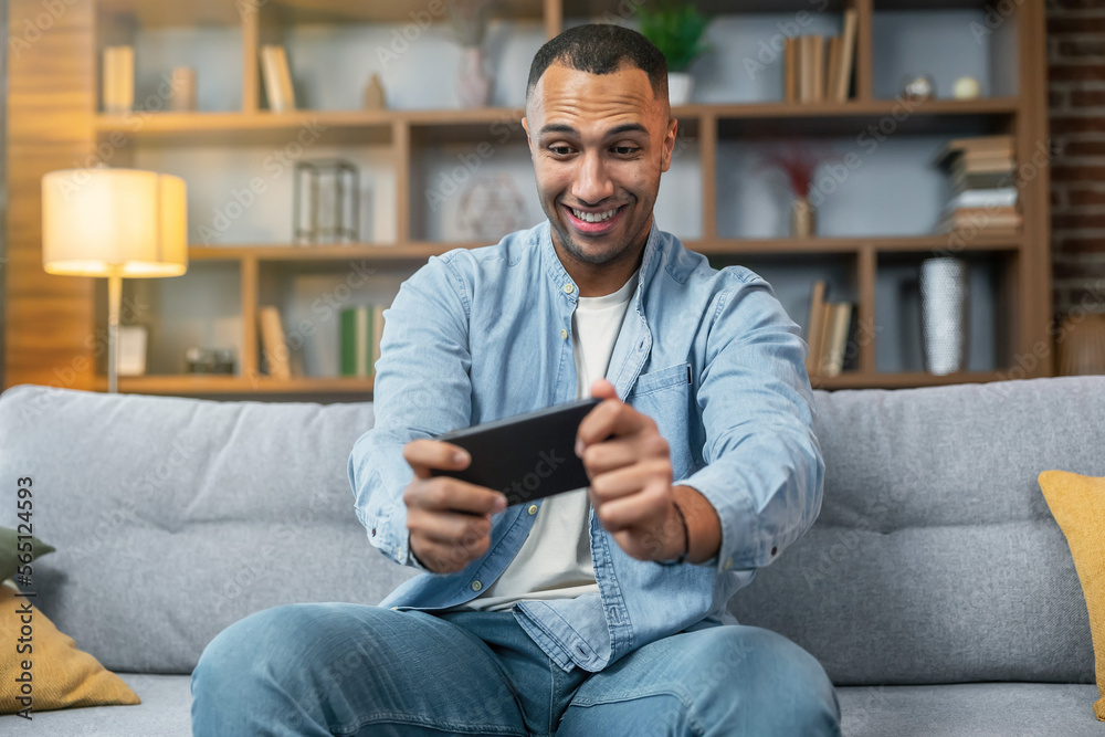 African american man playing video games on mobile phone, having fun with online gaming competition and working from home. Enjoying game play on smartphone, freelancer doing leisure activity. African american man playing video games on mobile phone, having fun with online gaming competition and working from home. Enjoying game play on smartphone, freelancer doing leisure activity.