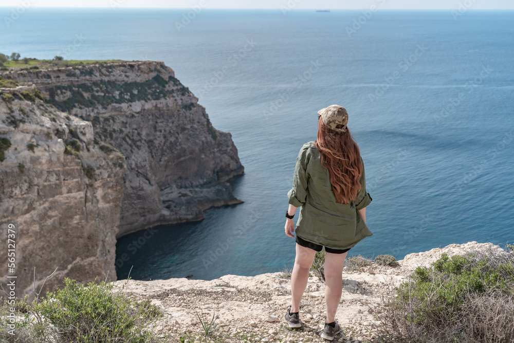 Woman standing on the cliff watching the sea on a sunny summer day in Malta