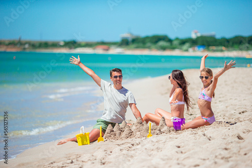 Parents and little daughter enjoying time on the beach. Family making sand castle together on the seashore