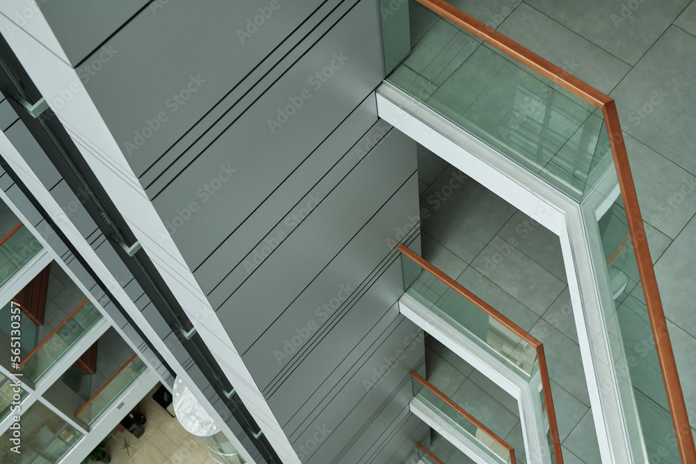 Above view of part of modern building interior with railings and transparent glass fencing decorating every storey Above view of part of modern building interior with railings and transparent glass fencing decorating every storey