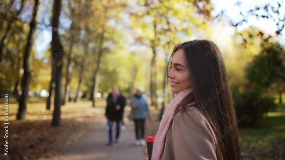 Young beautiful happy woman walks in autumn park, holding coffee in hands and joyfully jumps and revolve around yourself. Girl smile, enjoyment walk in nature. Model posing, looking in camera. Young beautiful happy woman walks in autumn park, holding coffee in hands and joyfully jumps and revolve around yourself. Girl smile, enjoyment walk in nature. Model posing, looking in camera.