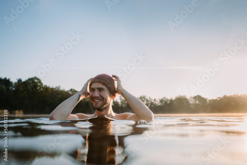 Young man soaks in the winter lake at morning. Male person taking care of his health