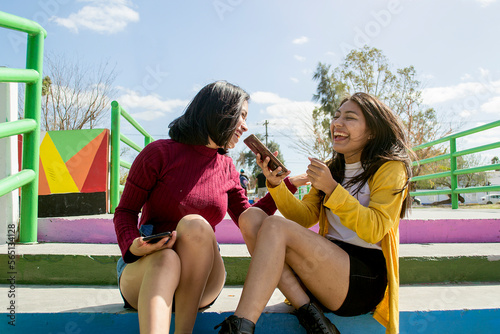 Amigas riendo sentadas en un parque. Chicas con celular