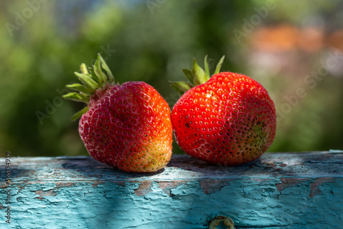 Two strawberries lie on a wooden table on a sunny summer day. Ripe red berries in sunlight closeup photo. Summer still life with strawberries.