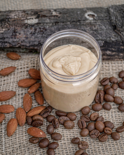  Natural handmade coffee and almond body butter with coffee beans and almond oil on beige and wooden background. Coffee and almond face cream  natural skin care.             