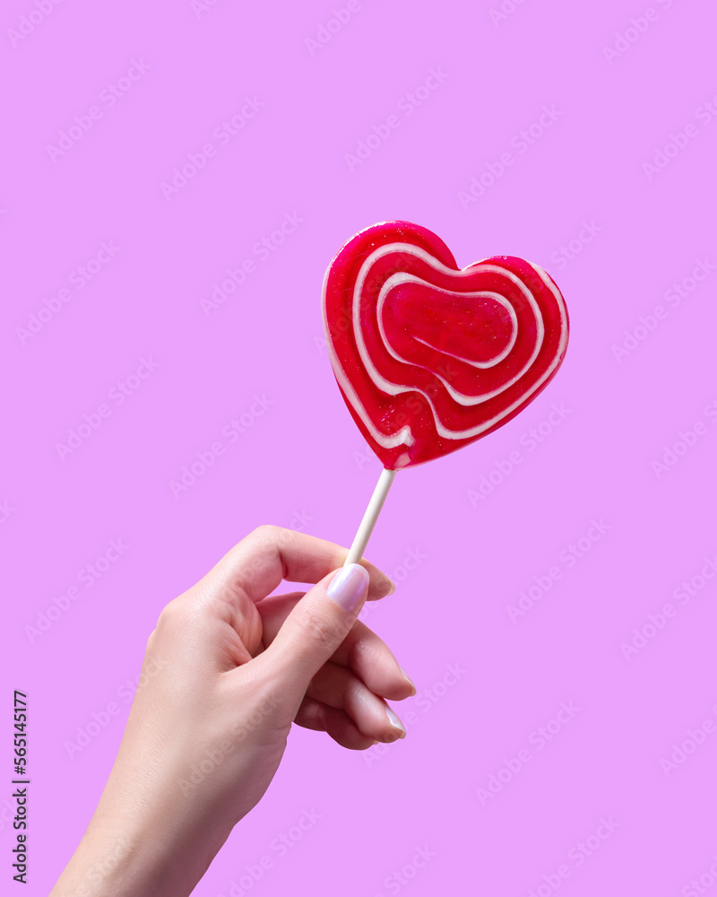 Woman hand holding red heart lollipop on pastel violet background