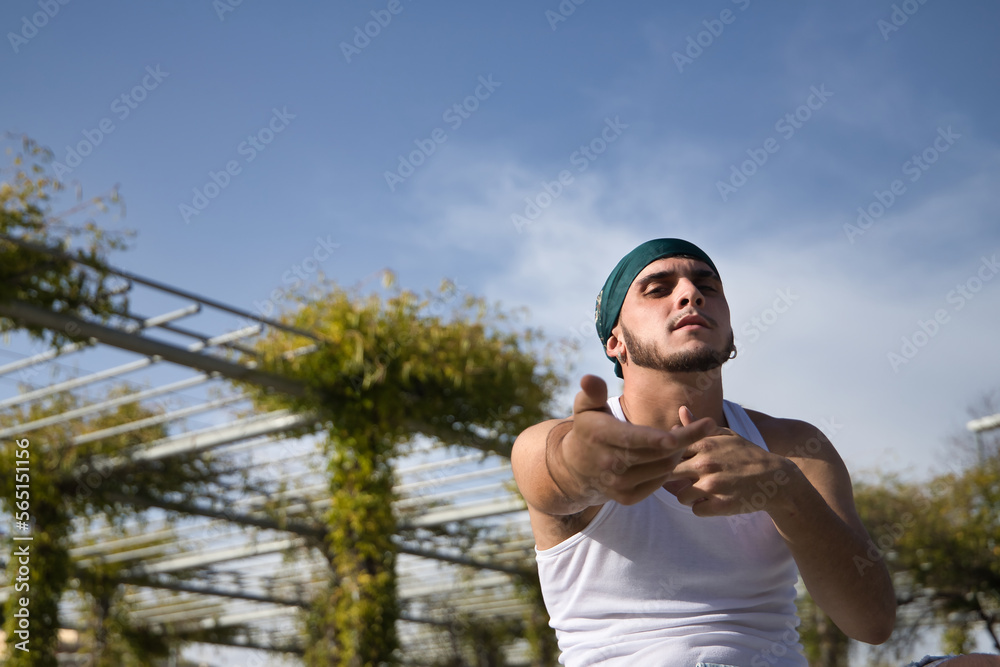 Latino and Hispanic boy, young, rebellious, wearing headscarf, looking defiantly at camera and gesturing as if rapping, sitting on a bench. Troubled concept, rebel, gangs, rapping, defiant. Latino and Hispanic boy, young, rebellious, wearing headscarf, looking defiantly at camera and gesturing as if rapping, sitting on a bench. Troubled concept, rebel, gangs, rapping, defiant.