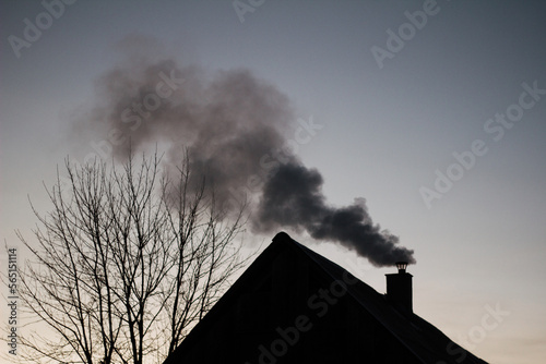 Dark smoke coming out the chimney on the roof in twilight, 