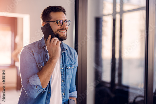 Handsome young man with glasses standing in the office and using the phone.