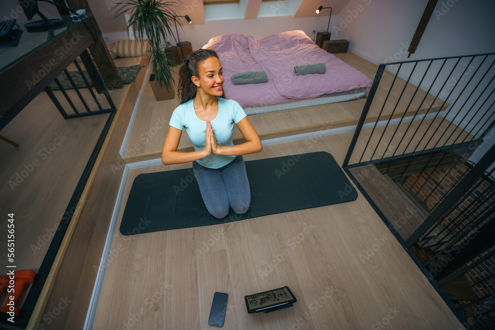 Woman doing yoga exercises while sitting on floor at home. Smiling healthy woman doing meditation exercises at home in living room Woman doing yoga exercises while sitting on floor at home. Smiling healthy woman doing meditation exercises at home in living room