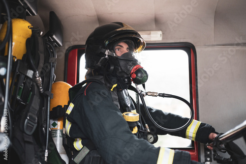 Profile view. A firefighter is sitting in the back of a uniformed fire truck wearing a gas mask prepared for emergency care.
