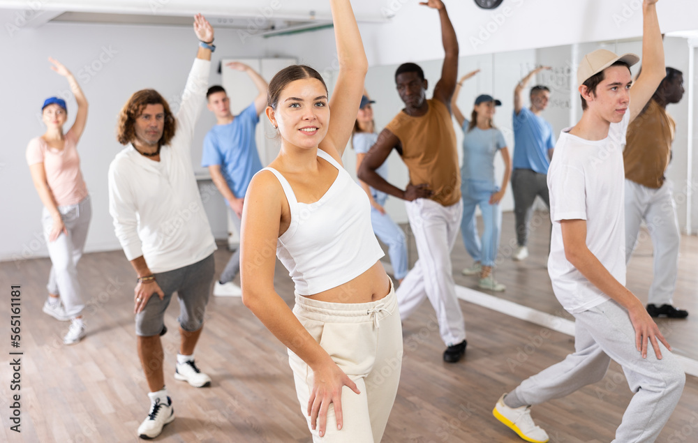 Group of young adult active multiethnic dancers stretching one arm up during learning new dance exercise movement in gym - obrazy, fototapety, plakaty 