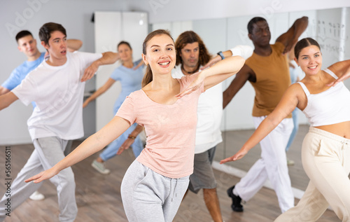 Joyful flexible multiethnic men and women exercising active moves with group of people in dance center