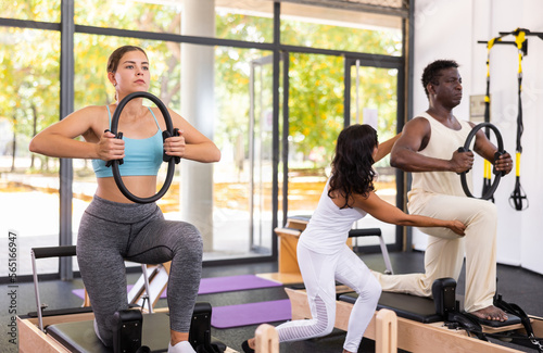 Latin female instructor helping active African American man during pilates training with ring to strengthen muscles in gym class