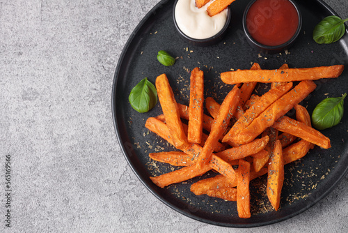 Top view of sweet potato sticks in a black plate with mayonnaise and ketchup sauce. Vegetarian food and healthy eating concept.