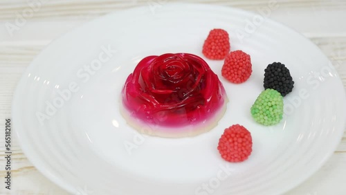 Rose shaped jelly dessert made from raspberries and cream in a white plate on a white wooden table. Decorative red, black and green raspberries.